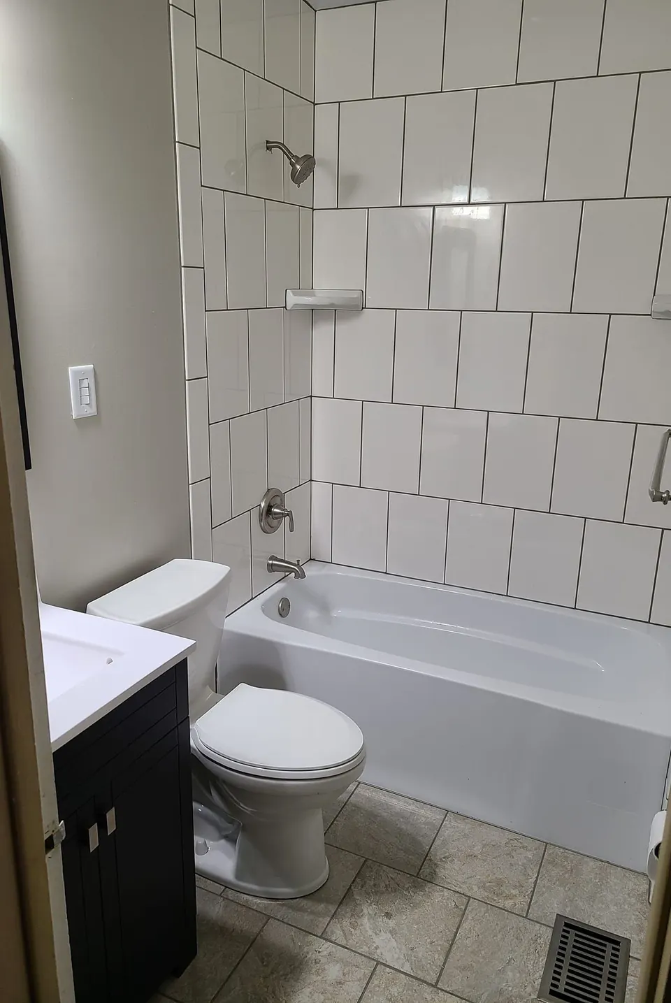 Renovated bathroom with a large white tile tub surround, brushed nickel fixtures and a dark vanity