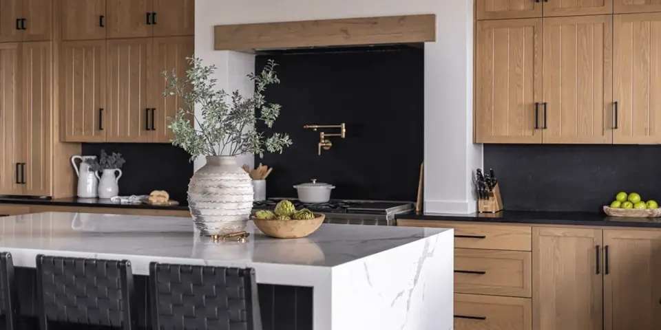 Kitchen with white oak cabinetry, a black stone backsplash and a waterfall marble island
