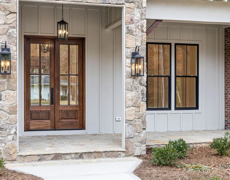 Stone and board-and-batten entry with stained double doors, lantern lights and black-framed windows
