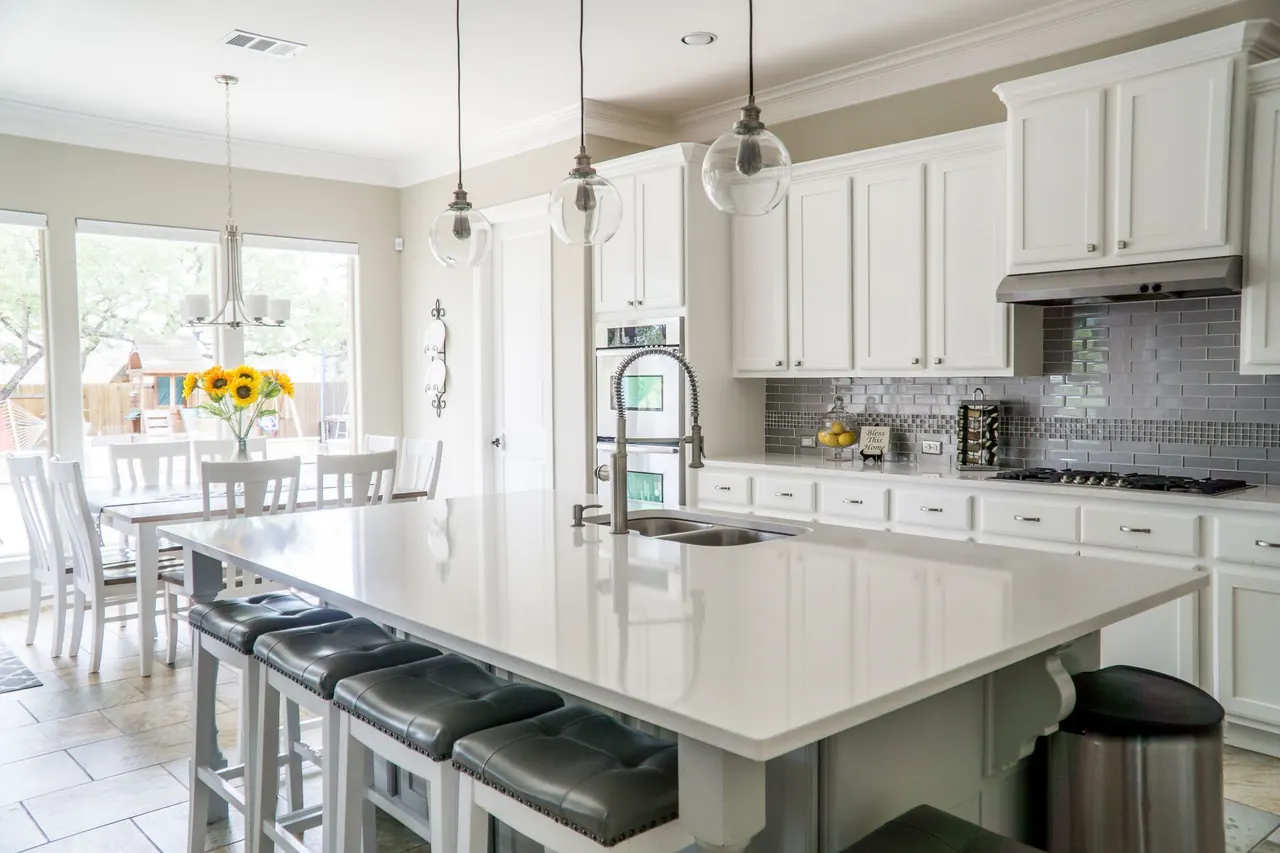 White kitchen with a long quartz island, pendant lights and a dining area by the windows